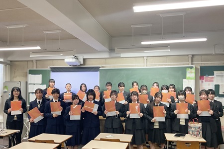 社会イノベーション学部２０周年記念ファイルをもった後藤准教授ゼミ生徒